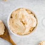 A bowl of peanut butter frosting on a table with a chocolate cake.