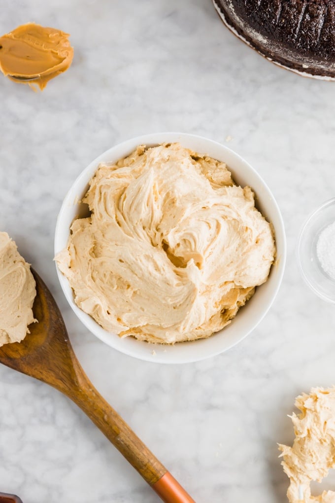 A bowl of peanut butter frosting on a table with a chocolate cake. 