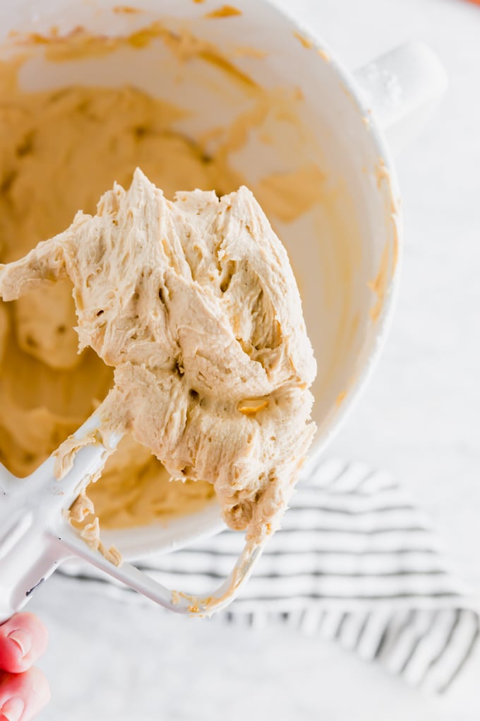 An electric mixer attachment with peanut butter frosting and a large mixing bowl. 