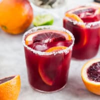 A photo of a blood orange margarita with slices of blood orange in the glass and a salted rim.