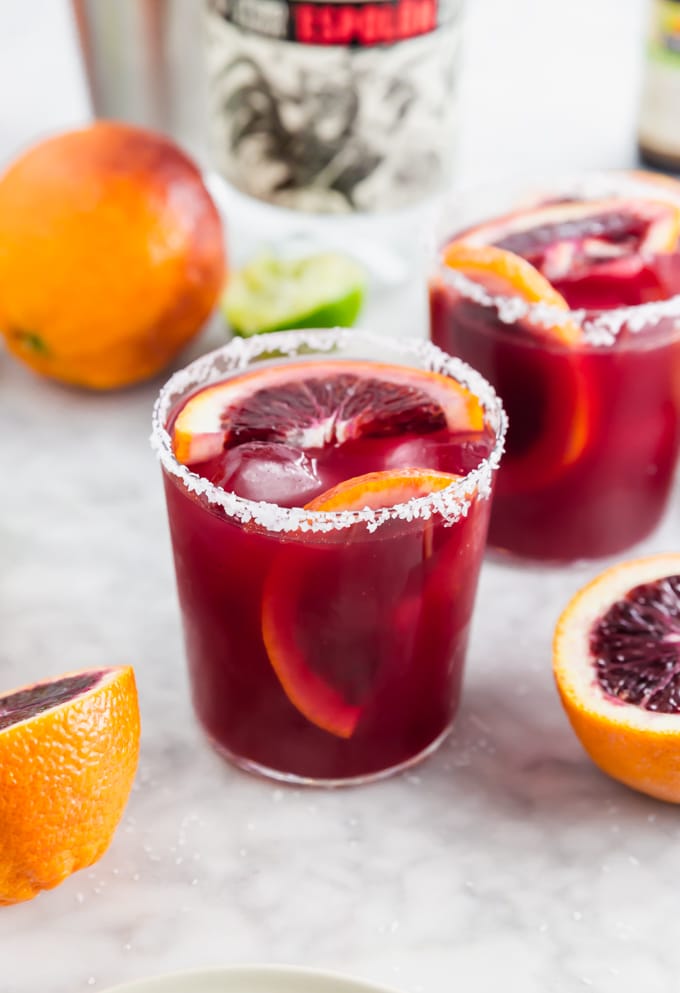 A photo of a blood orange margarita with slices of blood orange in the glass and a salted rim.