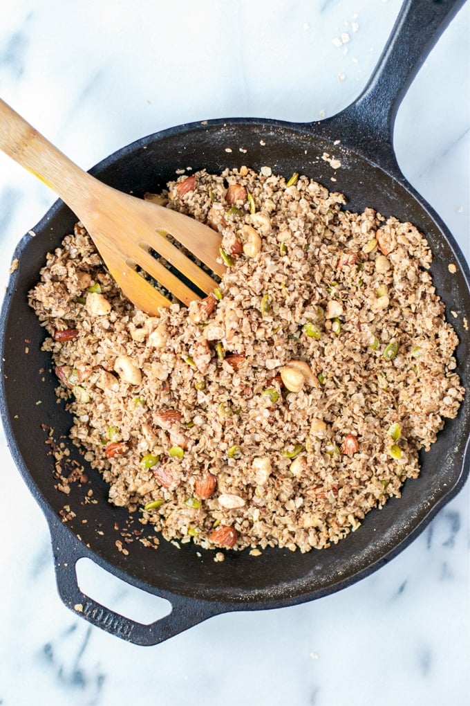 A skillet of granola with pumpkin seeds and almonds in it.