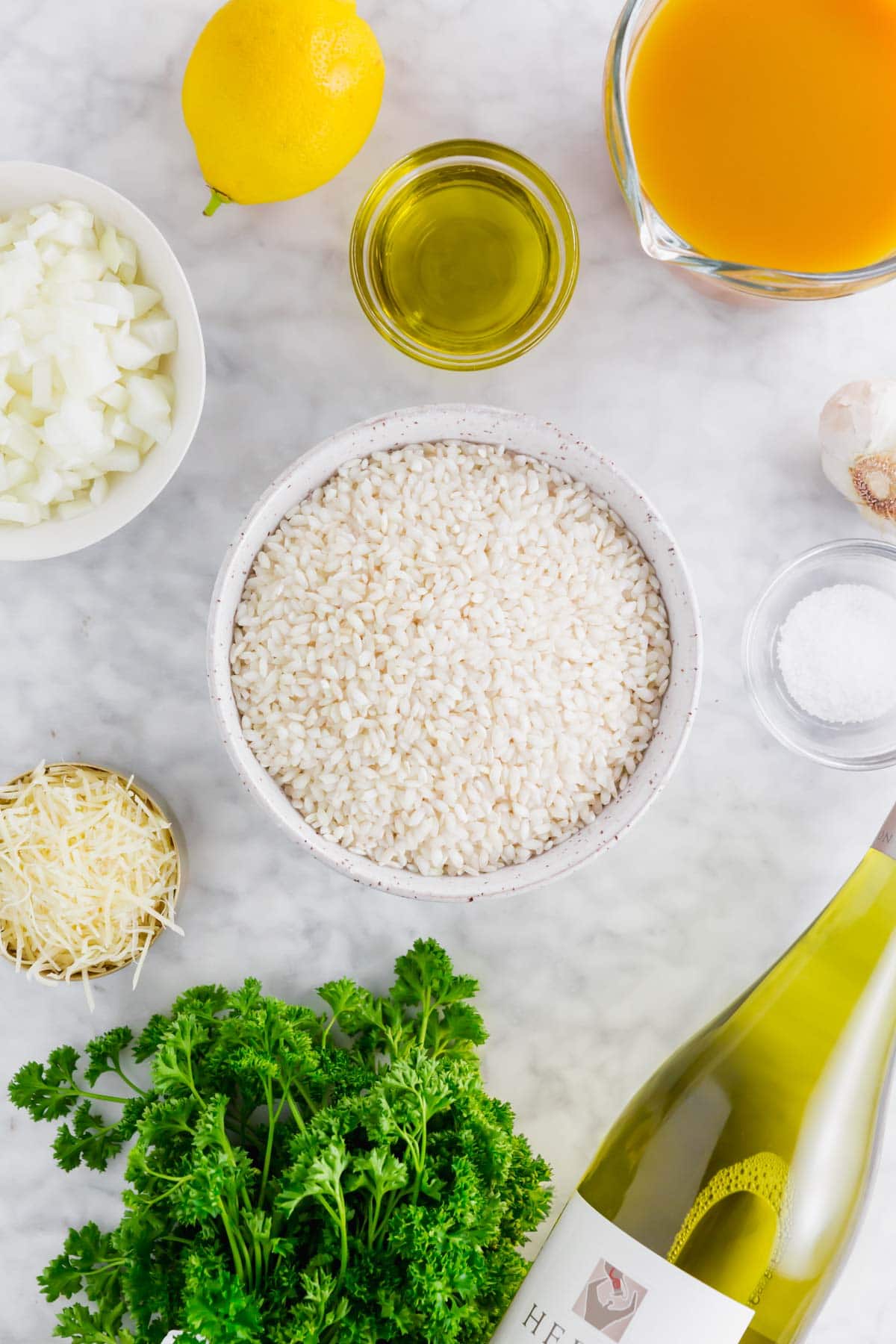 A photo of arborio rice, onion, lemon, olive oil, vegetable broth, garlic, wine and parsley to make instant pot lemon risotto.
