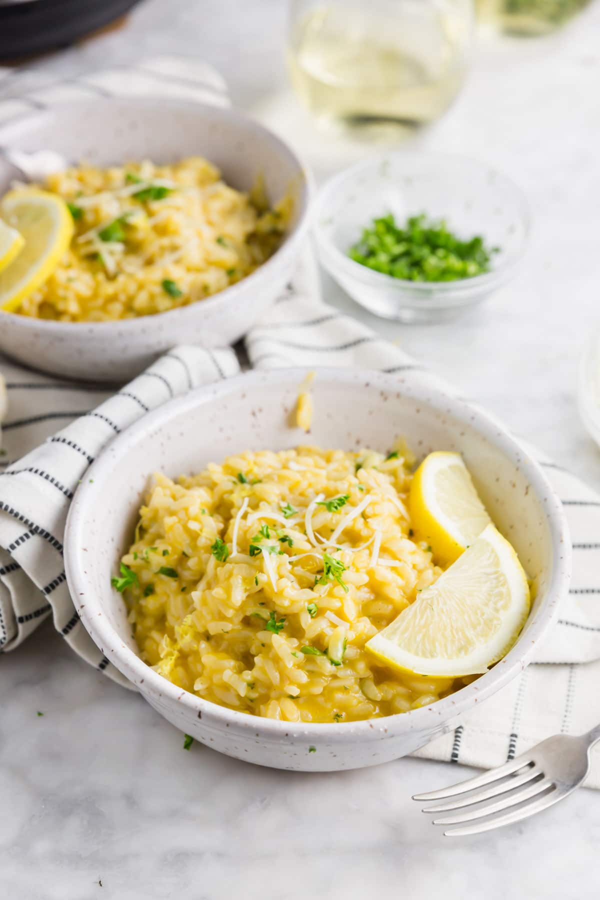 A photo of a bowl of instant pot lemon risotto topped with parsley, parmesan cheese and two lemon slices.