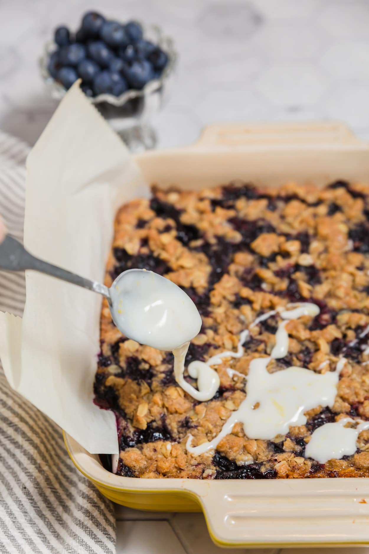 A spoon drizzling lemon glaze over gluten-free vegan blueberry pie bars.