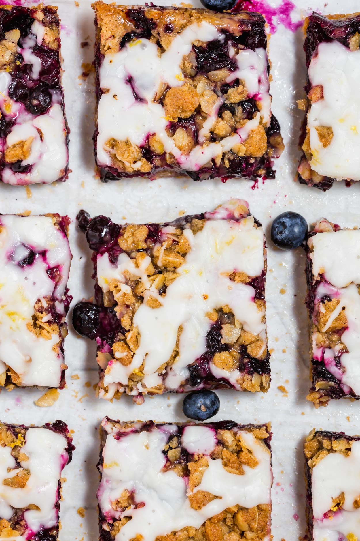 An overhead photo of nine gluten-free blueberry crumb bars with lemon glaze on a piece of parchment paper.