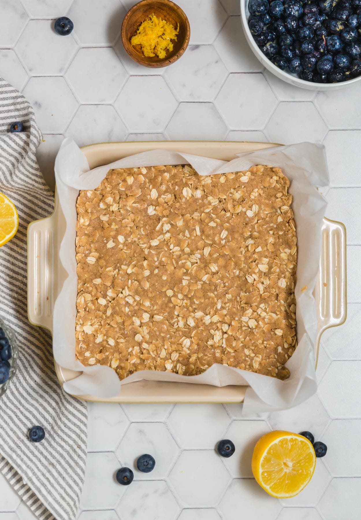 An overhead photo of an 8x8-inch baking dish lined with parchment paper and gluten-free crust for blueberry pie bars pressed into it.