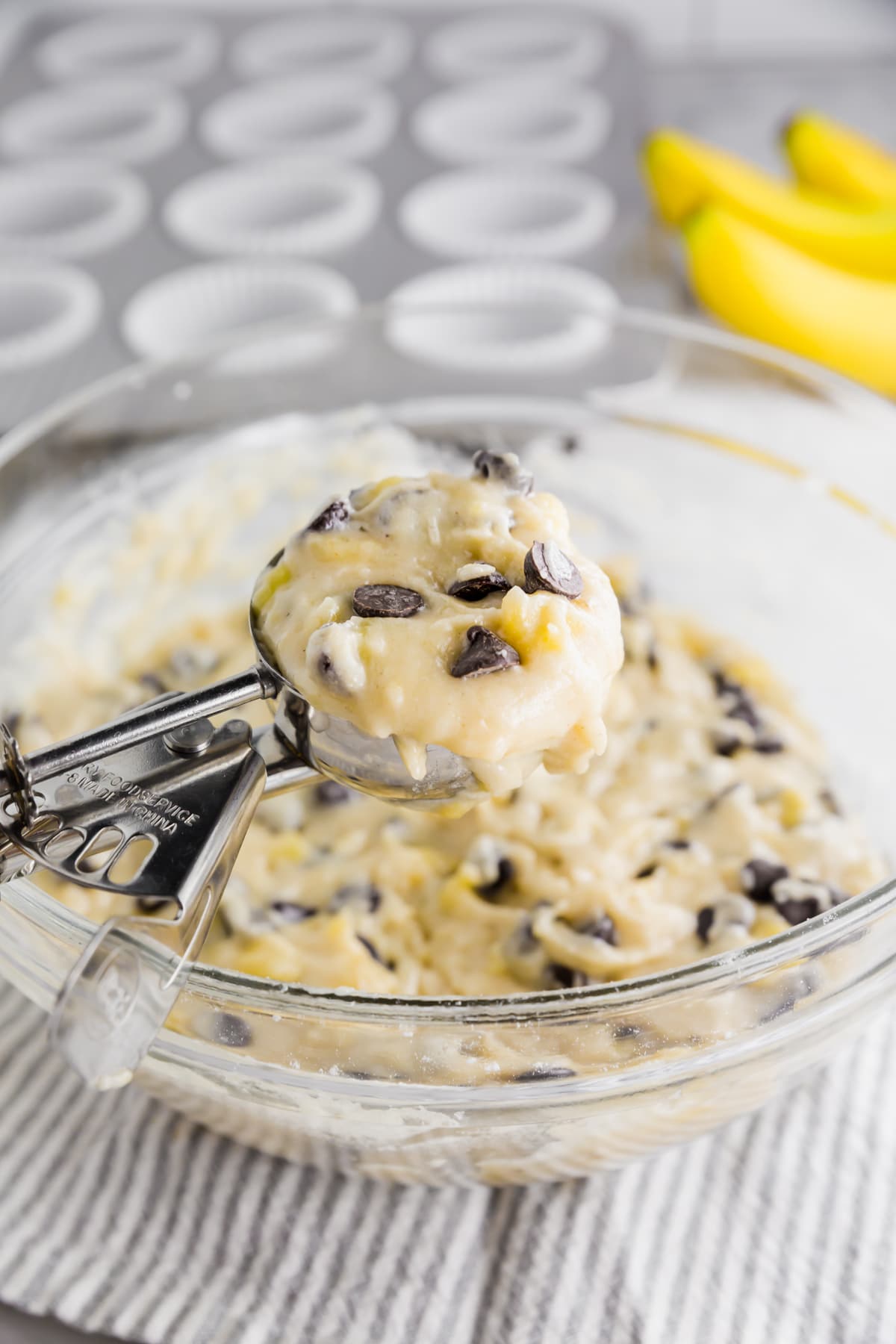 A cookie scoop with banana chocolate chip muffin batter in it ready to portion into a muffin tin.