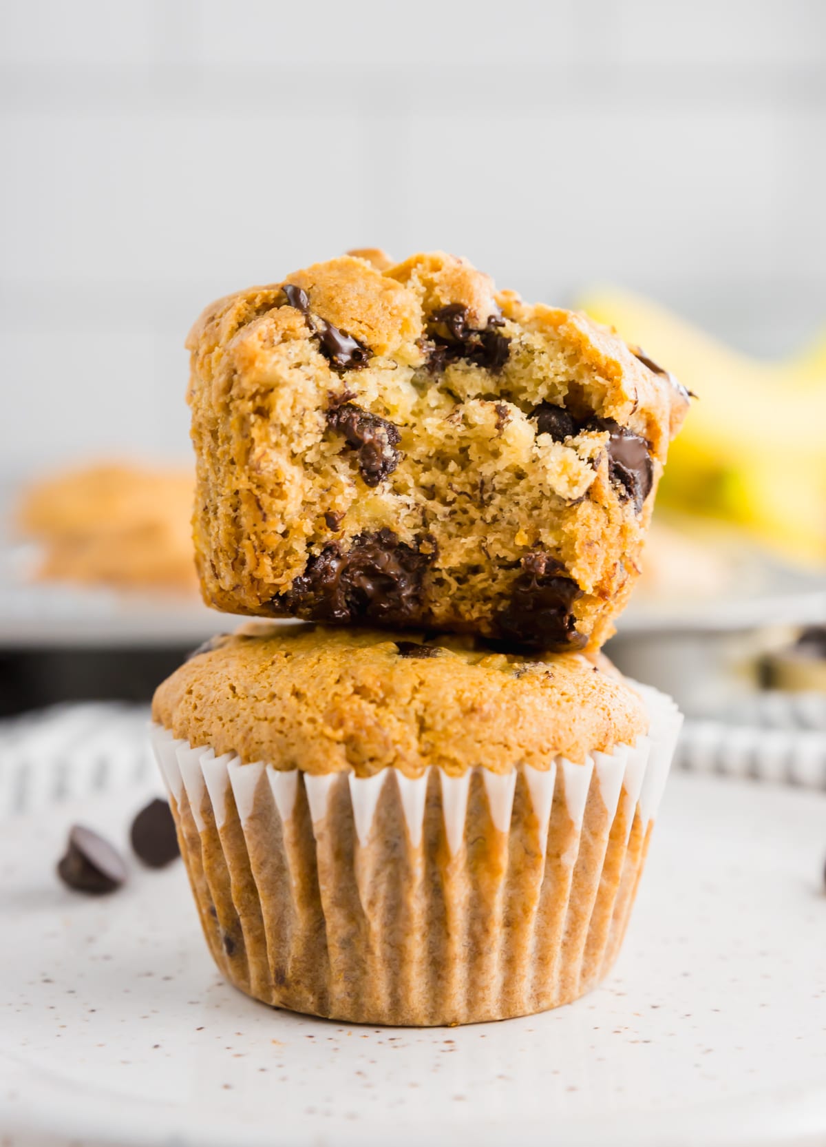 A stack of two banana chocolate chip muffins with the top one cut in half.