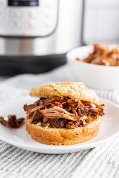 A photo of a BBQ Pulled pork sandwich with BBQ sauce and an Instant Pot in the background.