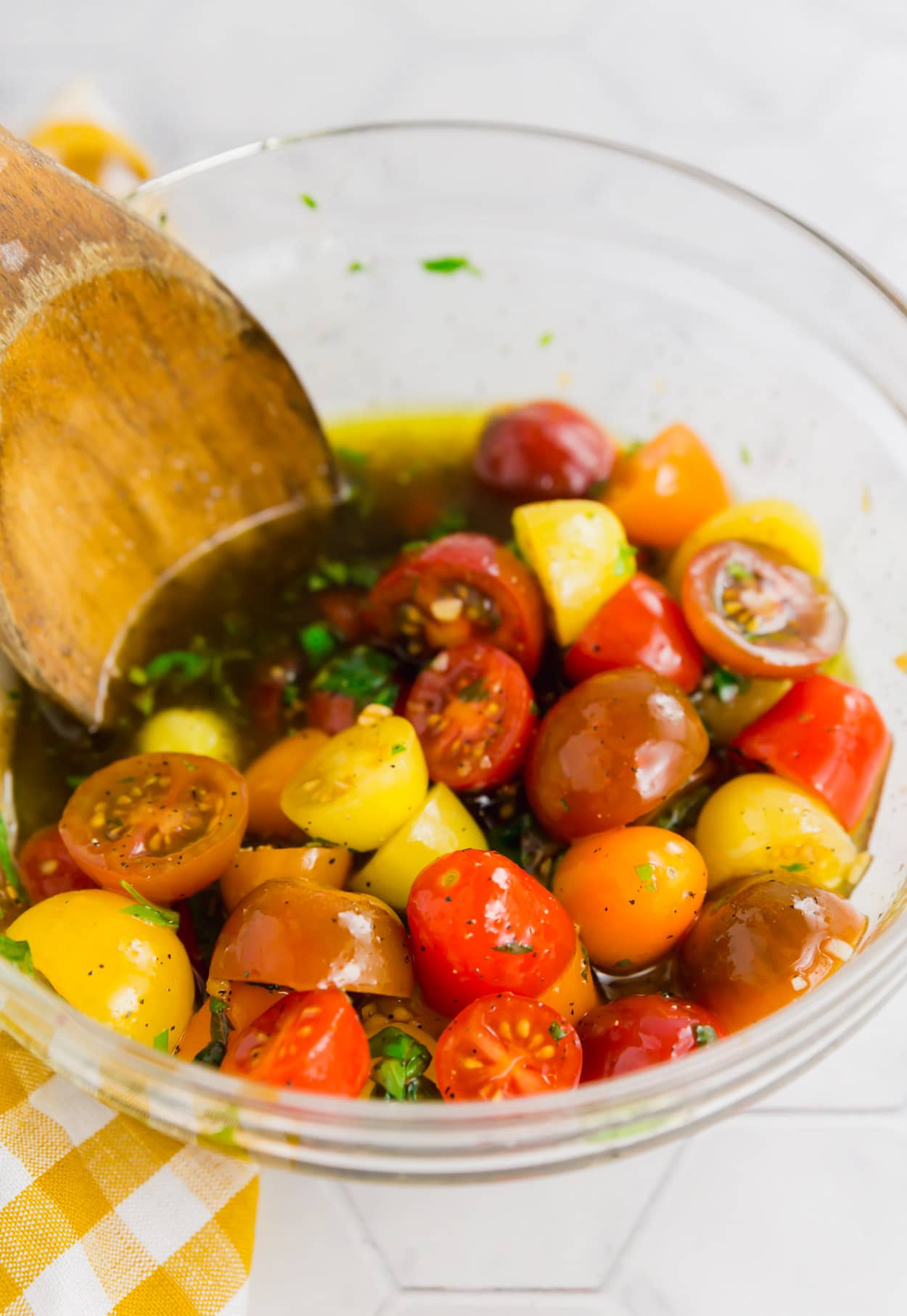 A photo of a mixing bowl with colorful cherry tomatoes, olive oil, balsamic vinegar and fresh basil ready to be mixed.