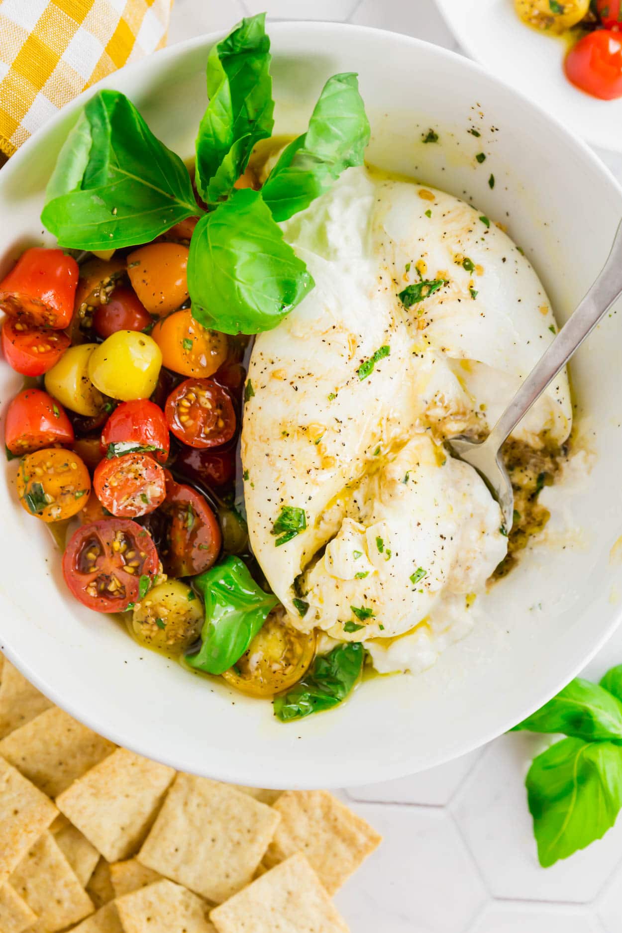 An overhead photo of marinated cherry tomatoes, fresh basil, and burrata in a bowl with a drizzle of olive oil.