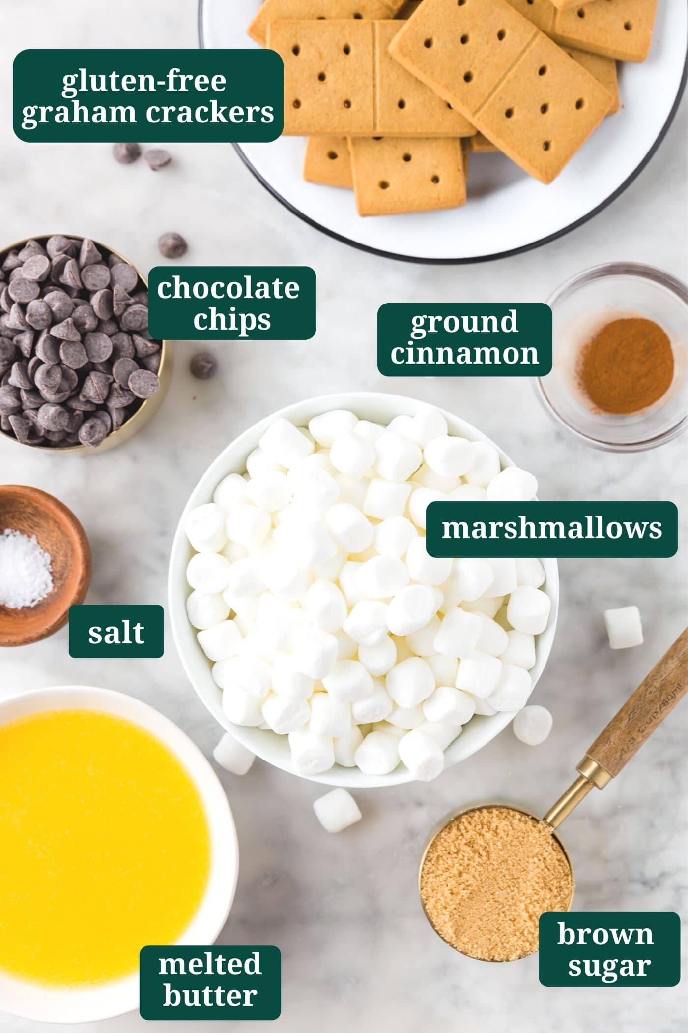 An overhead photo of ingredients for s'mores bars: gluten-free graham crackers, semi-sweet chocolate chips, mini marshmallows, ground cinnamon, salt, melted butter and brown sugar.