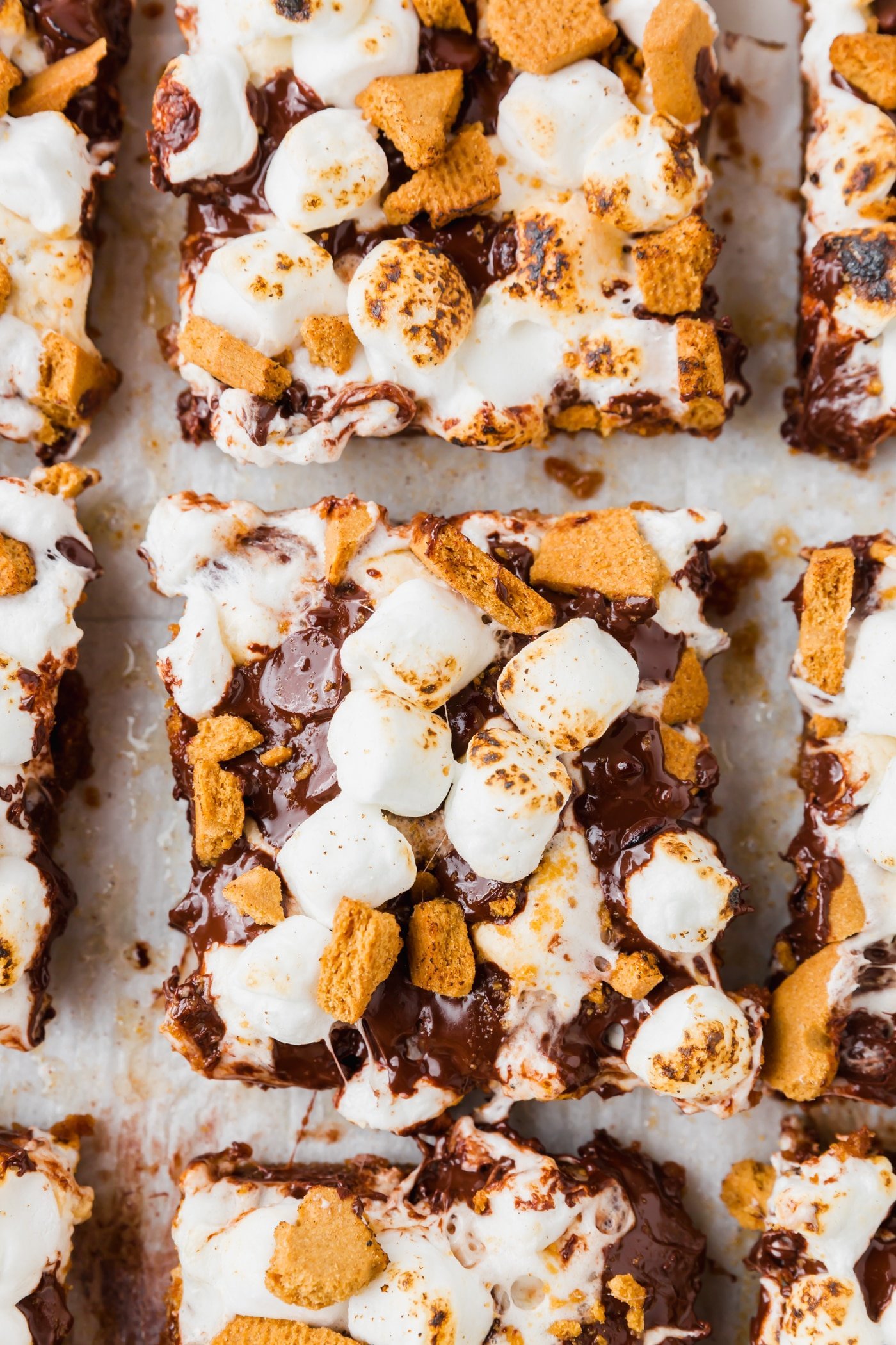 An overhead view of sliced gluten-free smores bars topped with graham crackers and marshmallows on a piece of parchment paper. 