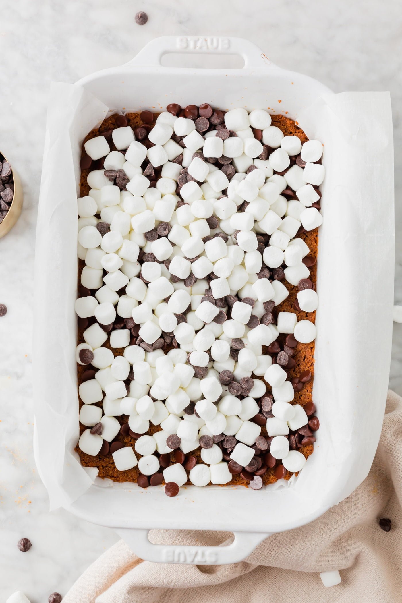 A baking dish with graham cracker crust, chocolate chips and marshmallows in it.