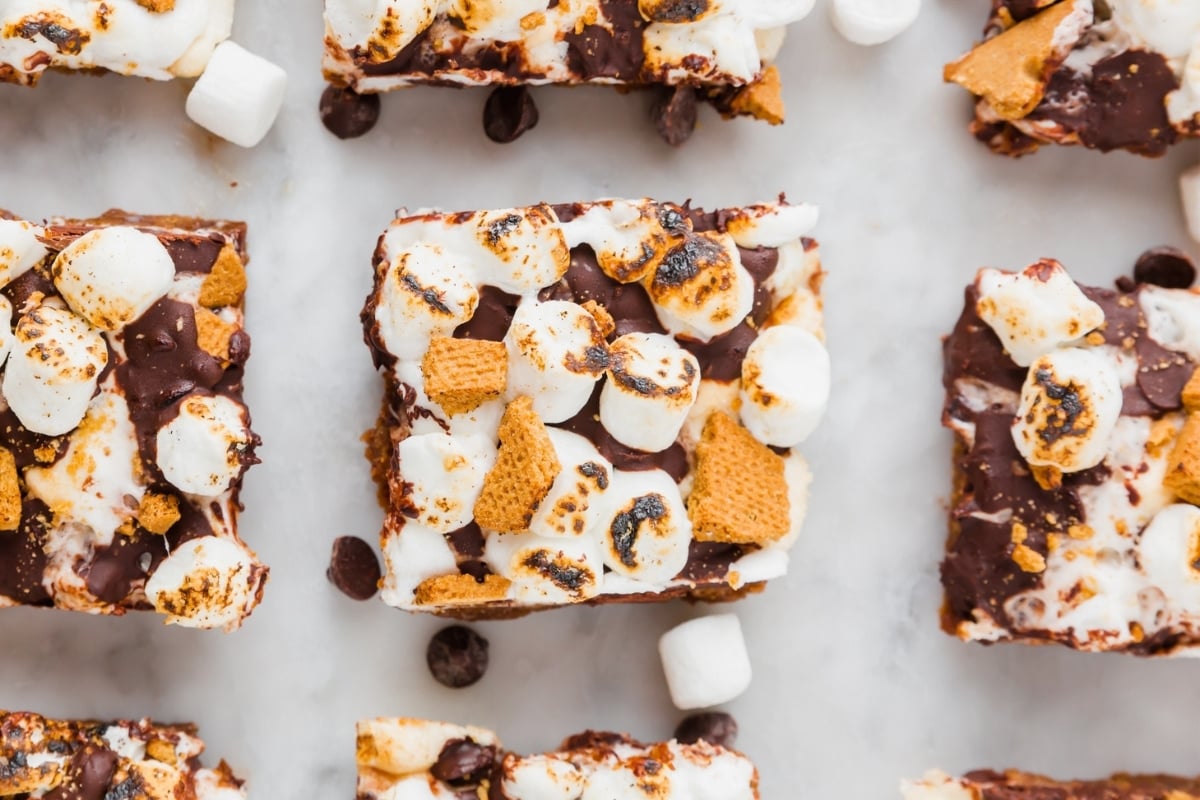 Top-down view of Gluten-Free S’mores Bars topped with toasted marshmallows, melted chocolate, and graham cracker pieces, arranged on a light surface.