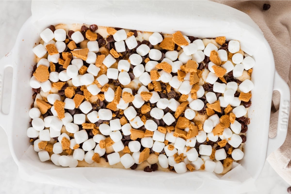 A baking dish filled with Gluten-Free S’mores Bars, topped with mini marshmallows, chocolate chips, and crumbled gluten-free graham crackers, seen from above.