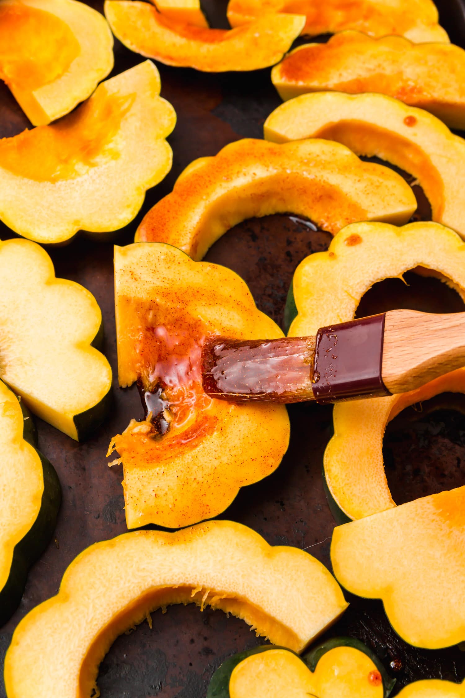 Sliced acorn squash being brushed with maple syrup and spices.