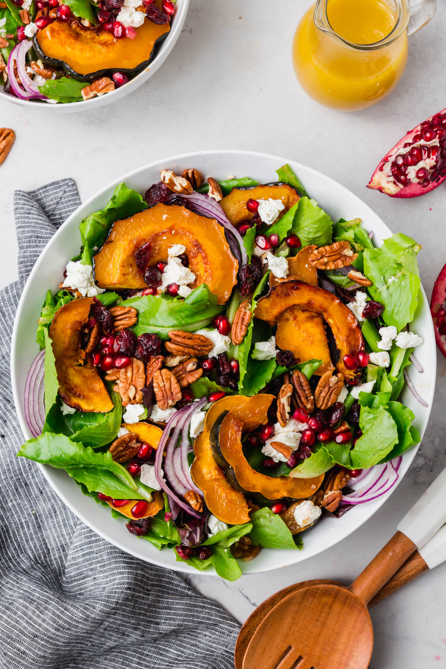 Overhead shot of a bowl of fall salad with pomegranate, acorn squash, goat cheese, red onions and mixed greens in a bowl