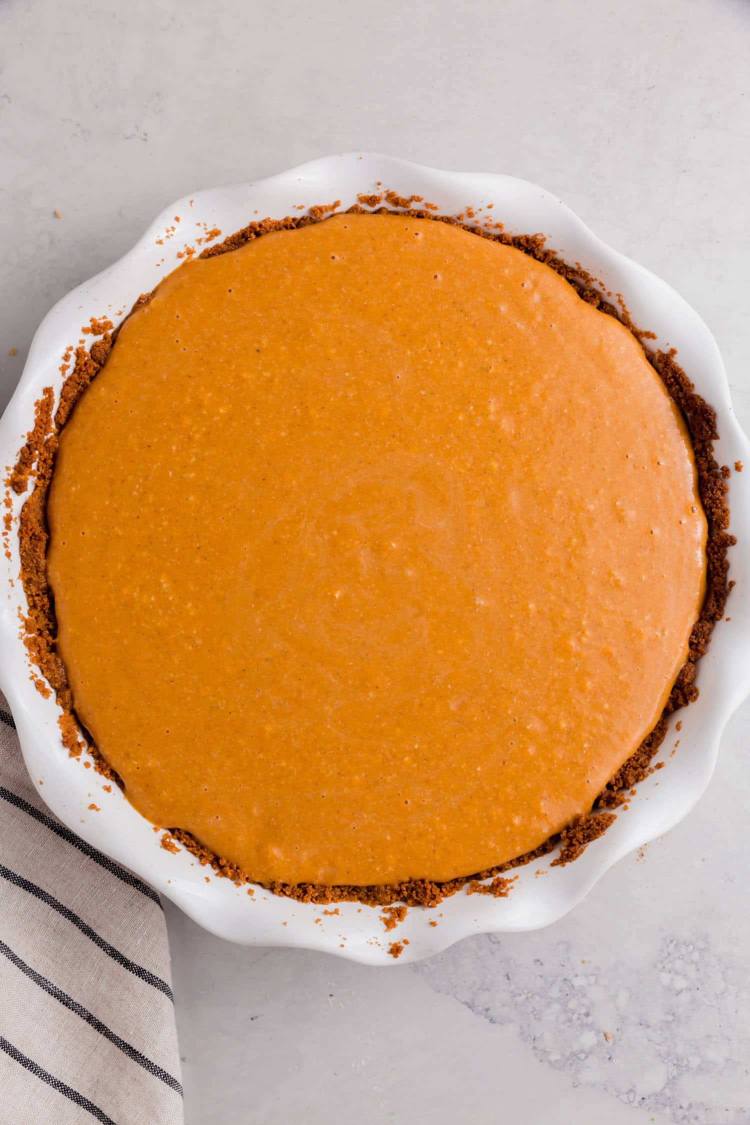 A gluten-free graham cracker crust filled with pumpkin pie filling ready for the oven.