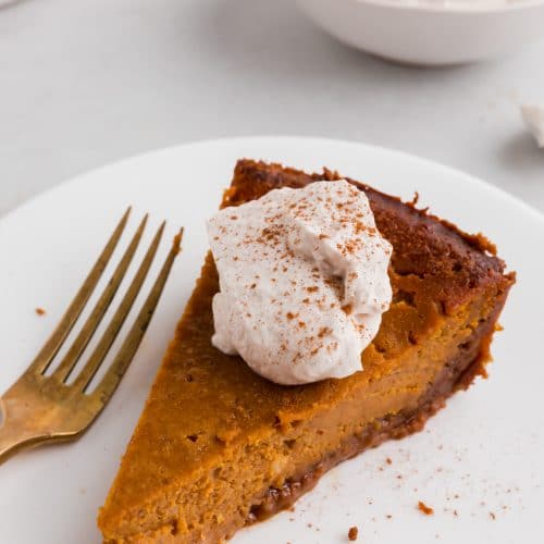 A photo of a slice of pumpkin pie with gluten-free graham cracker crust with a dollop of whipped cream and sprinkle of cinnamon on it.