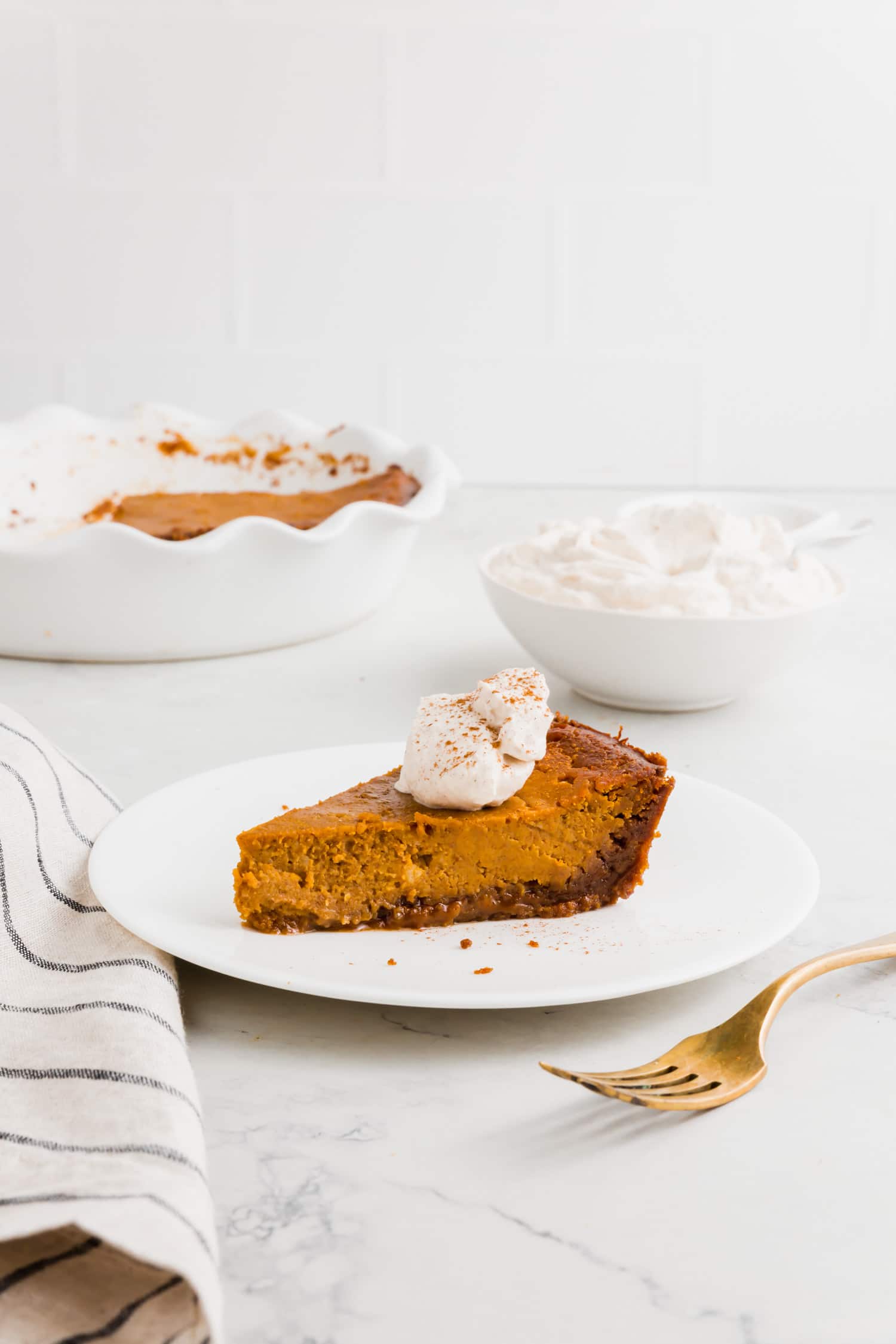 A photo showing a piece of pumpkin pie with gluten-free graham cracker crust on a plate with a dollop of whipped cream on top.