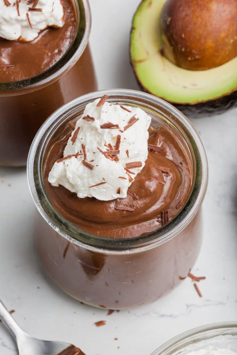 Two small jars of chocolate vocado pudding topped with shaved chocolate and a dollop of whipped cream.