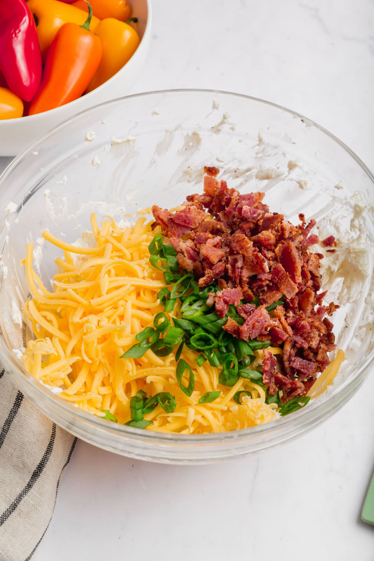 A large glass bowl with shredded cheddar cheese, cooked bacon bits, and sliced green onion.