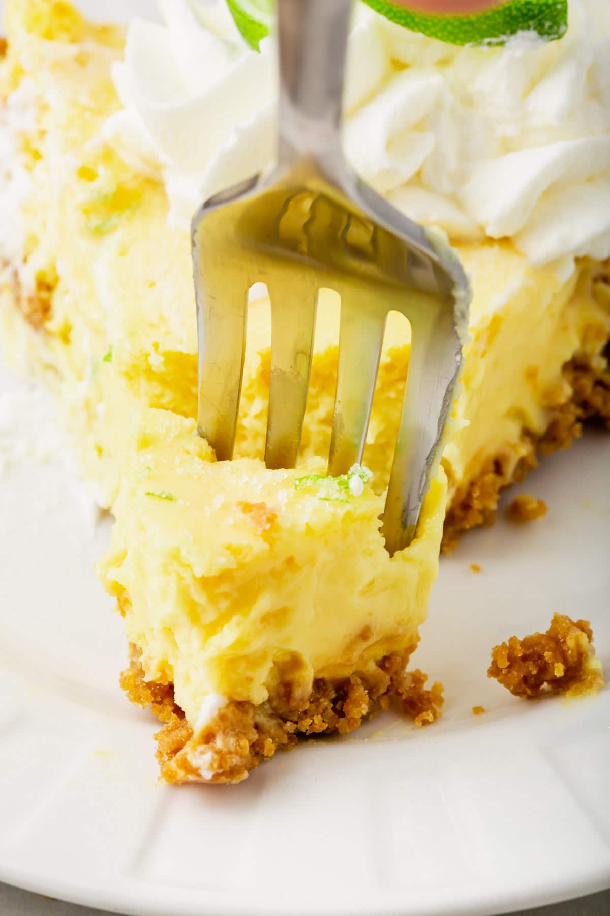 A close-up of a fork breaking off a bite of key lime pie.