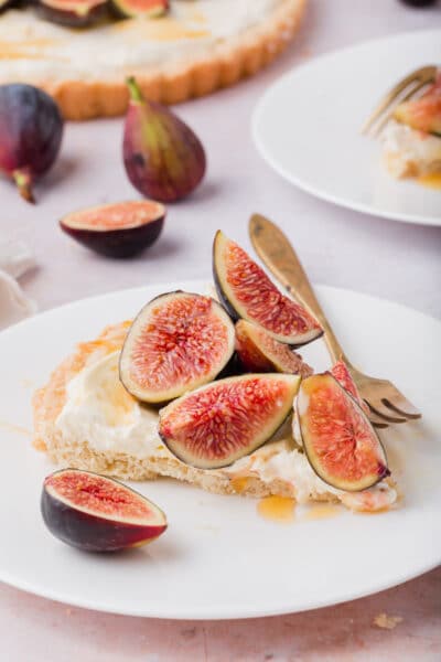 Slice of tart on a plate with fresh figs on top and a drizzle of honey.