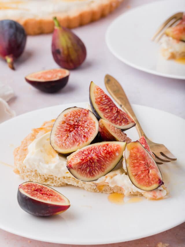 Slice of tart on a plate with fresh figs on top and a drizzle of honey.