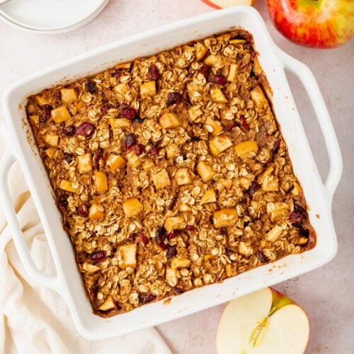 A tray of gluten-free vegan apple baked oatmeal next to a couple of apples on a table.