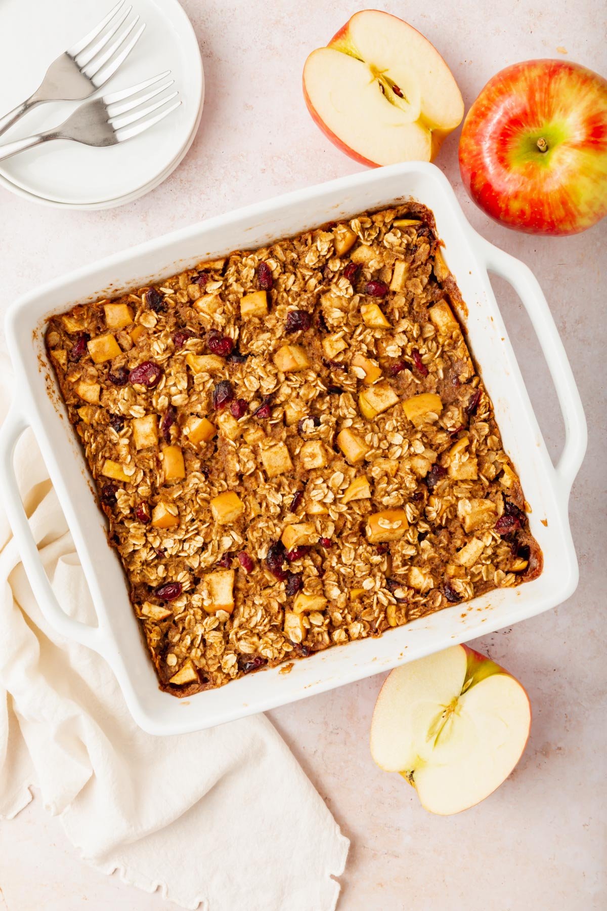 A tray of gluten-free vegan apple baked oatmeal next to a couple of apples on a table.