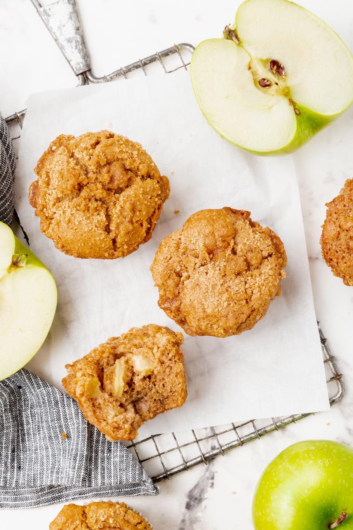Gluten-free vegan apple cinnamon muffins on a table with green apples.