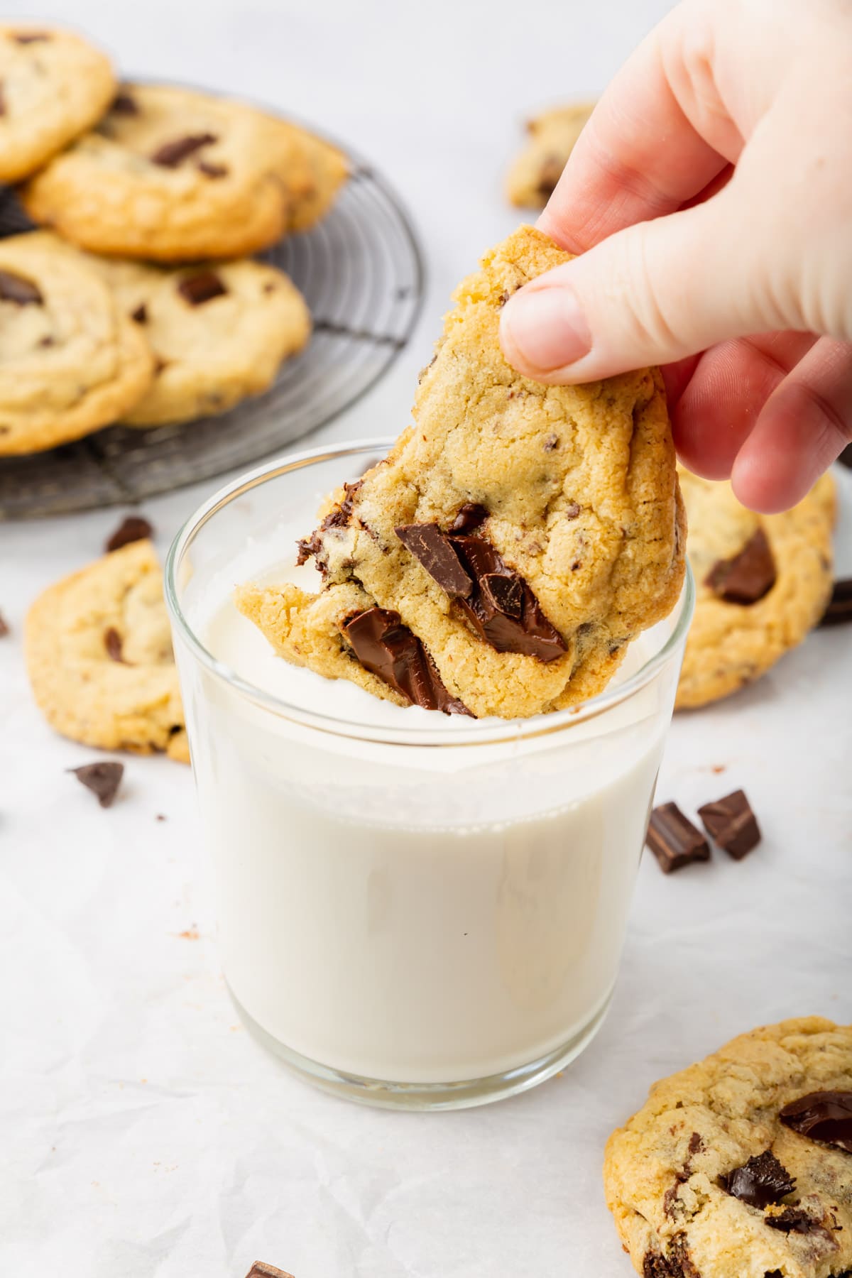 A hand holding and dipping a gluten-free chocolate chip cookie in a glass of milk.