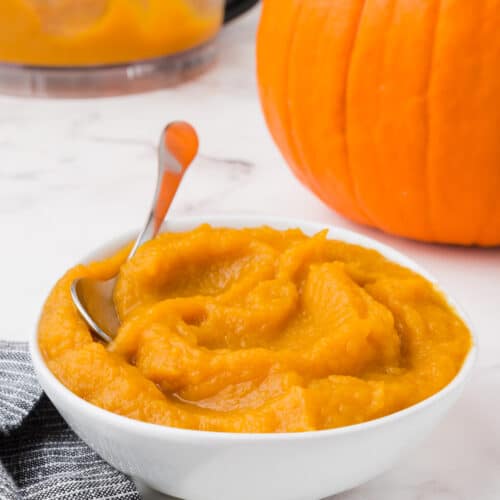 A bowl of pumpkin puree with a pumpkin in the background.
