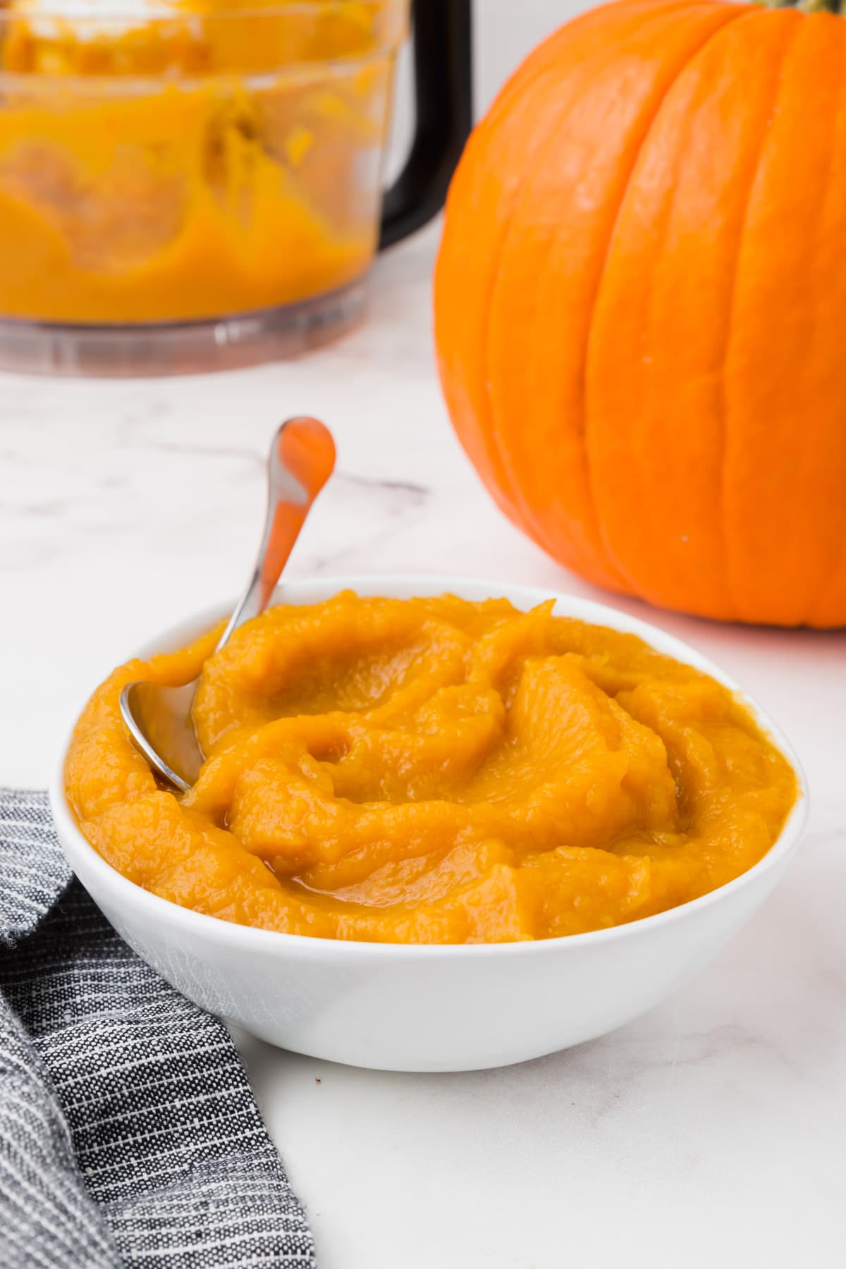 A bowl of pumpkin puree with a pumpkin in the background.