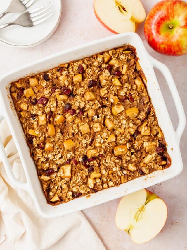 A tray of gluten-free vegan apple baked oatmeal next to a couple of apples on a table.