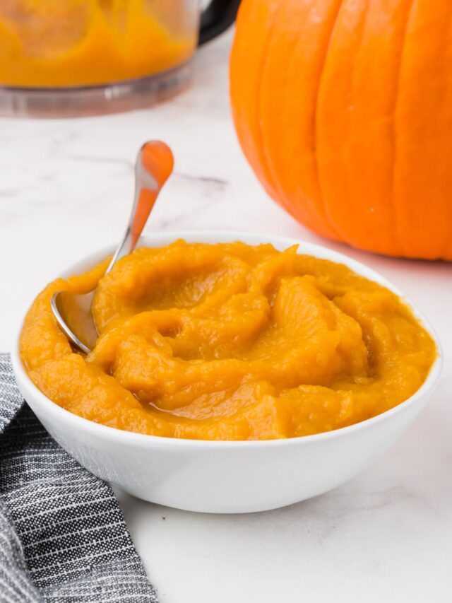 A bowl of pumpkin puree with a pumpkin in the background.