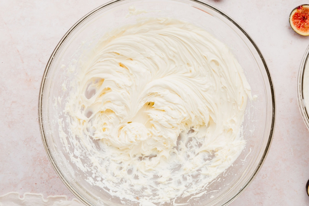 A glass bowl filled with whipped mascarpone cheese mixture, swirled smoothly with peaks, sits on a light countertop—perfect as a filling for a gluten-free fig tart.