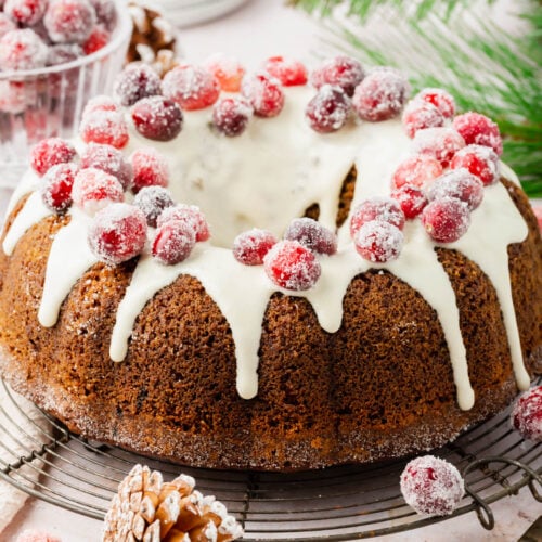 Gluten-free gingerbread bundt cake with a frosted glaze and sugared cranberries on a platter.