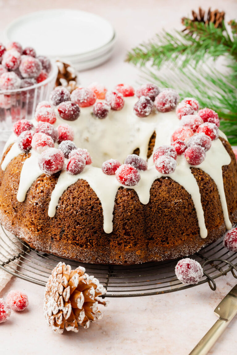 Gluten-free gingerbread bundt cake with a frosted glaze and sugared cranberries on a platter.