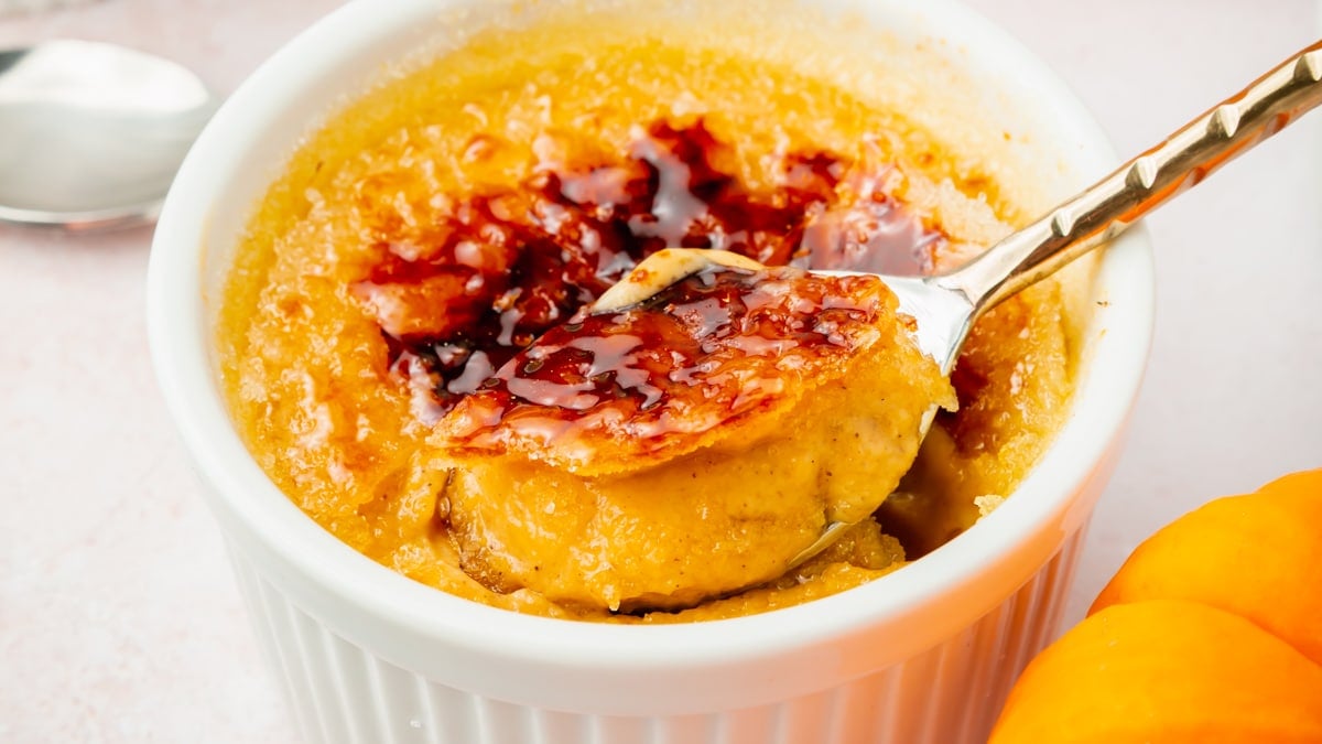 A closeup of a spoon scooping some pumpkin creme brulee out of a ramekin.