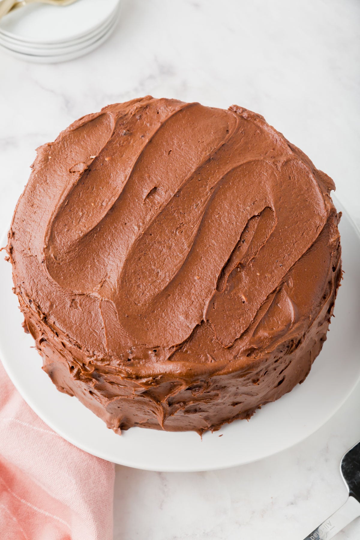 A gluten-free chocolate cake with chocolate frosting on a cake stand.