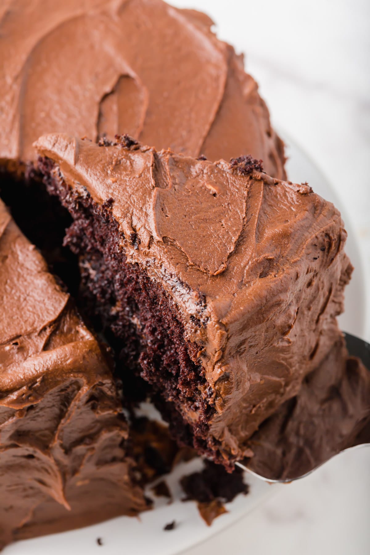 A slice of a gluten-free chocolate cake with chocolate frosting being lifted from the cake.