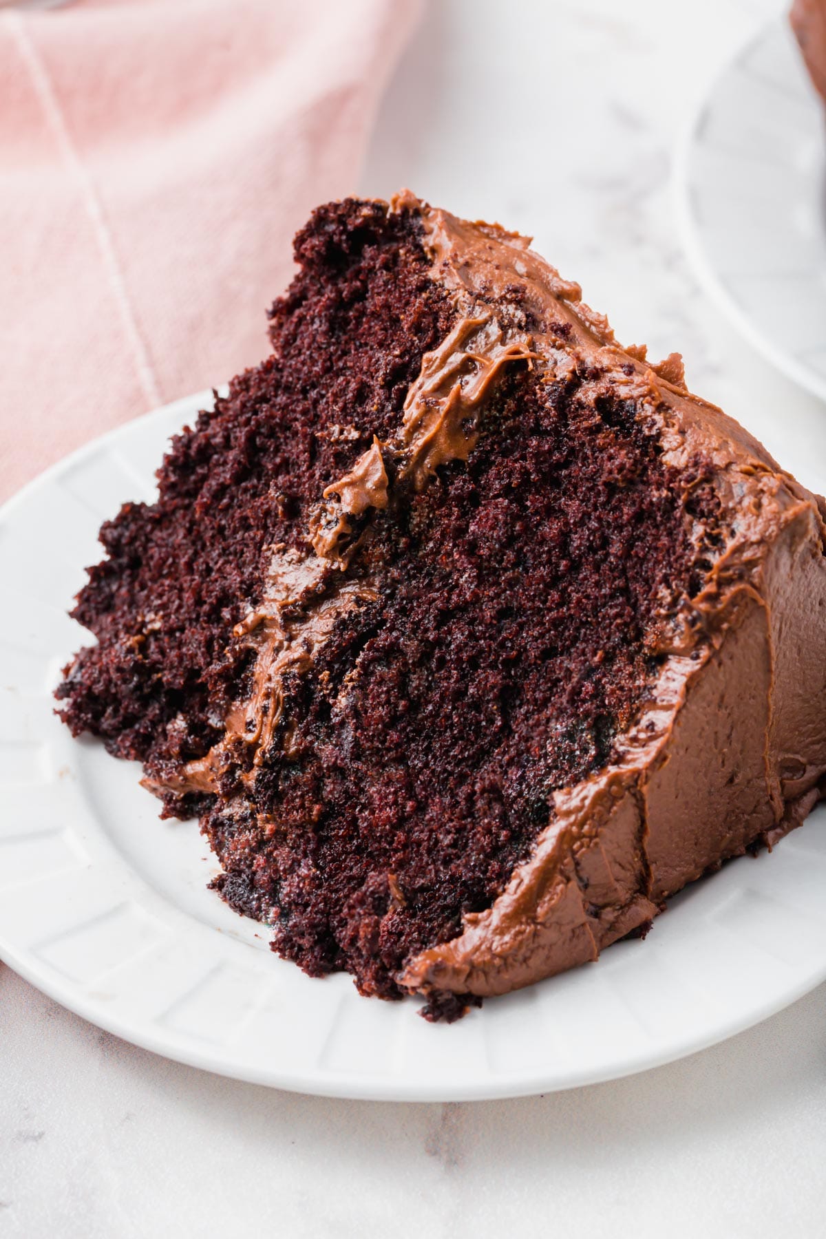 A slice of a gluten-free chocolate cake with chocolate frosting on a plate.