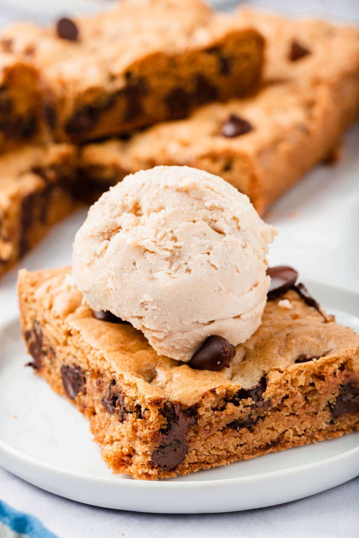 A square of gluten-free chocolate chip cookie bar topped with a scoop of ice cream.