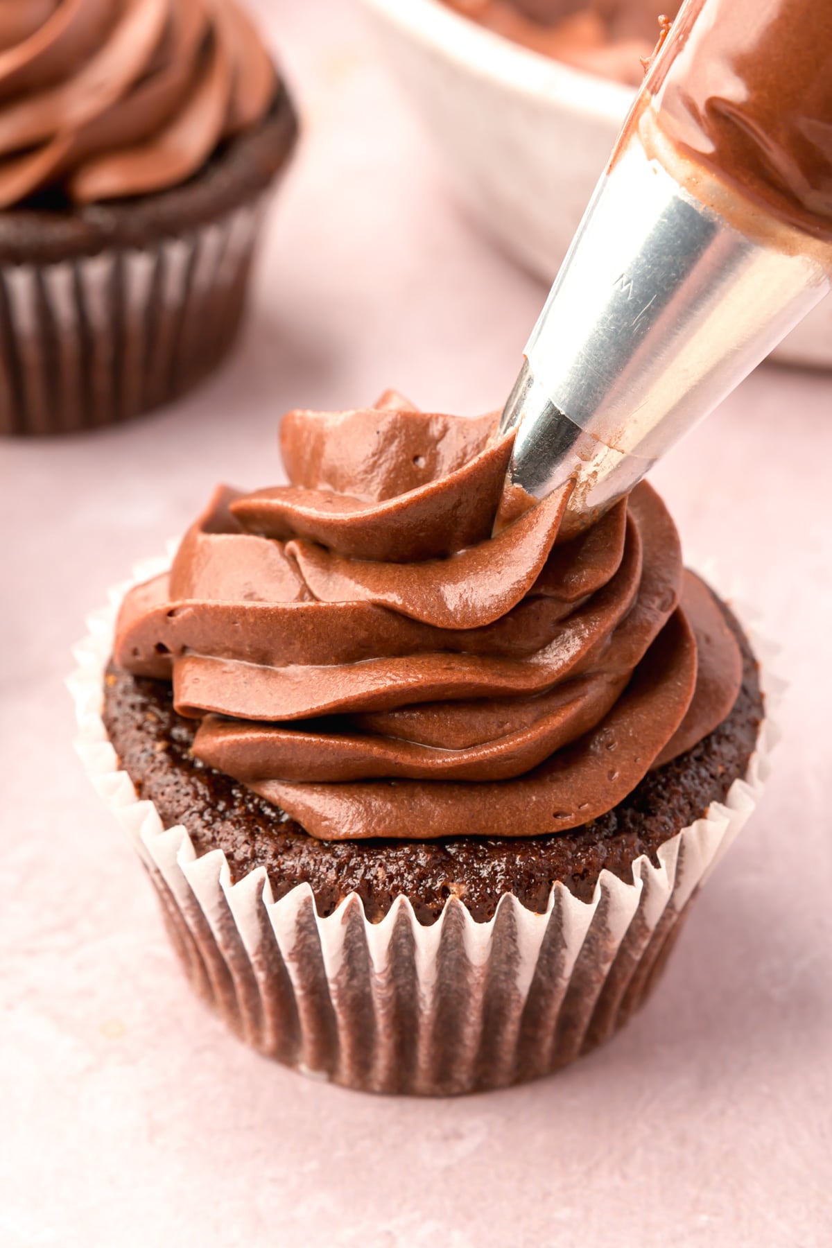 Chocolate cream cheese frosting being piped onto a chocolate cupcake.