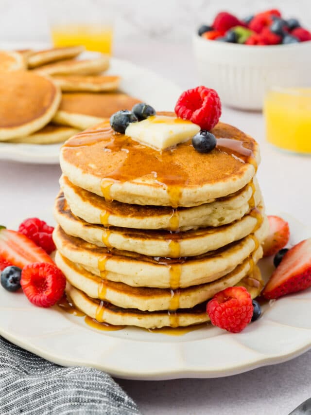 A stack of gluten-free pancakes topped with butter, fresh berries, and maple syrup.