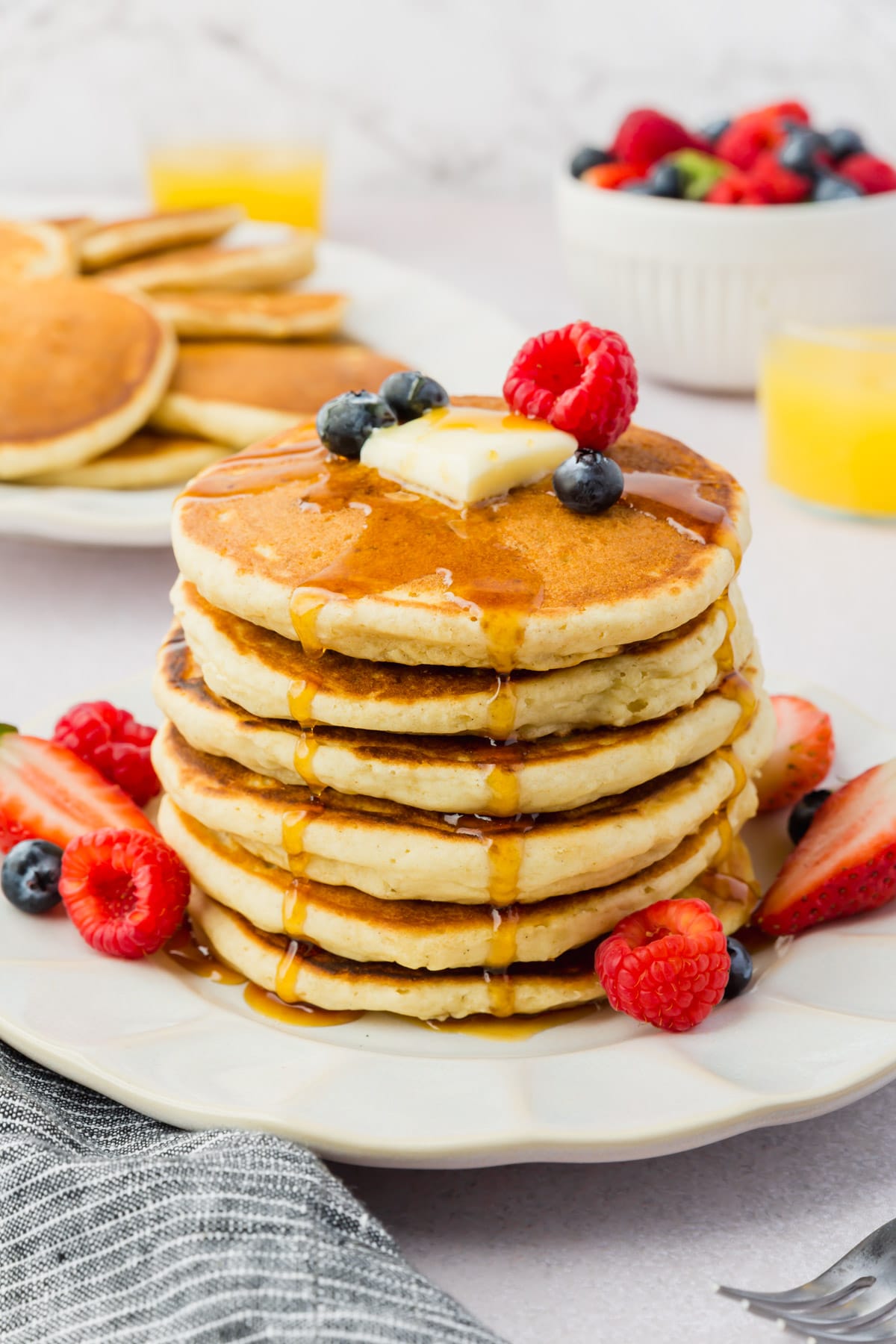 A stack of gluten-free pancakes topped with butter, fresh berries, and maple syrup.